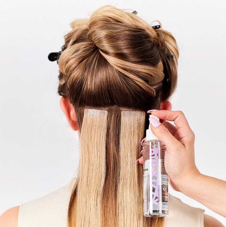 Hair extensions being applied to a woman's styled hair with a spray bottle.