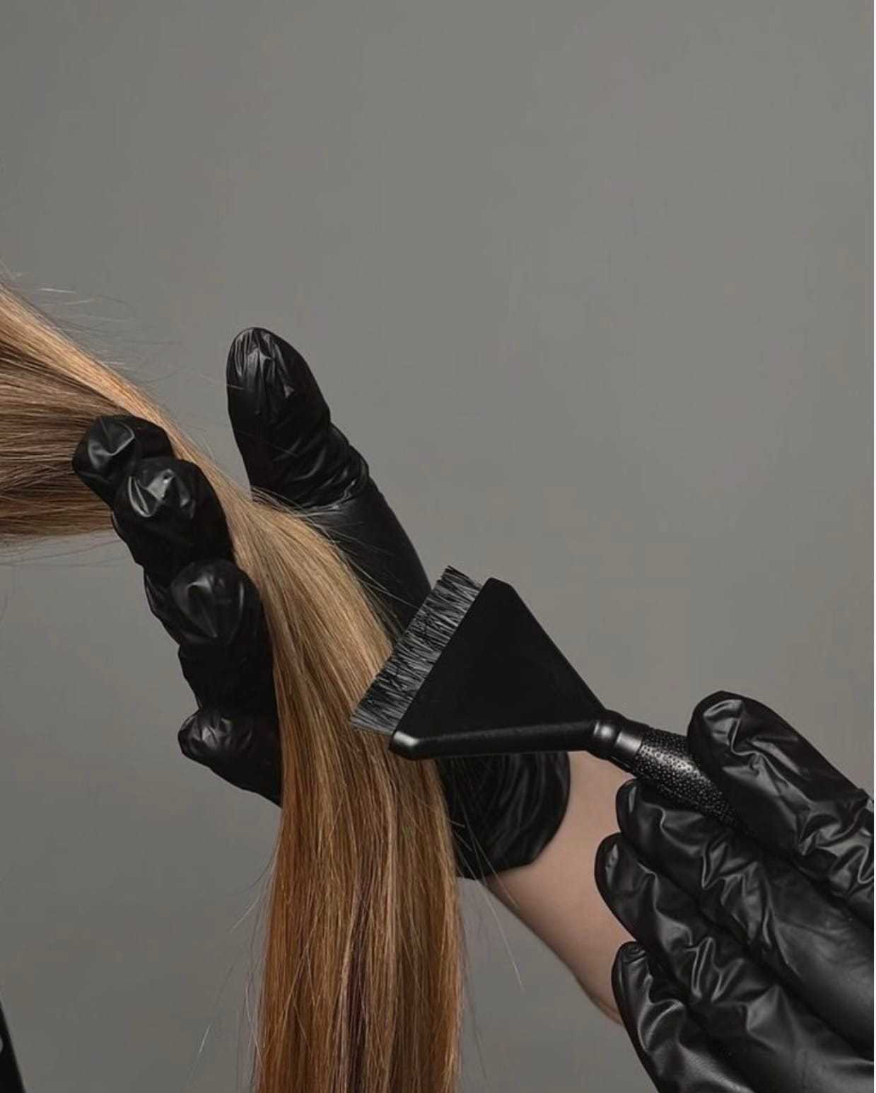 Hair stylist in black gloves applying dye to brown hair with brush.