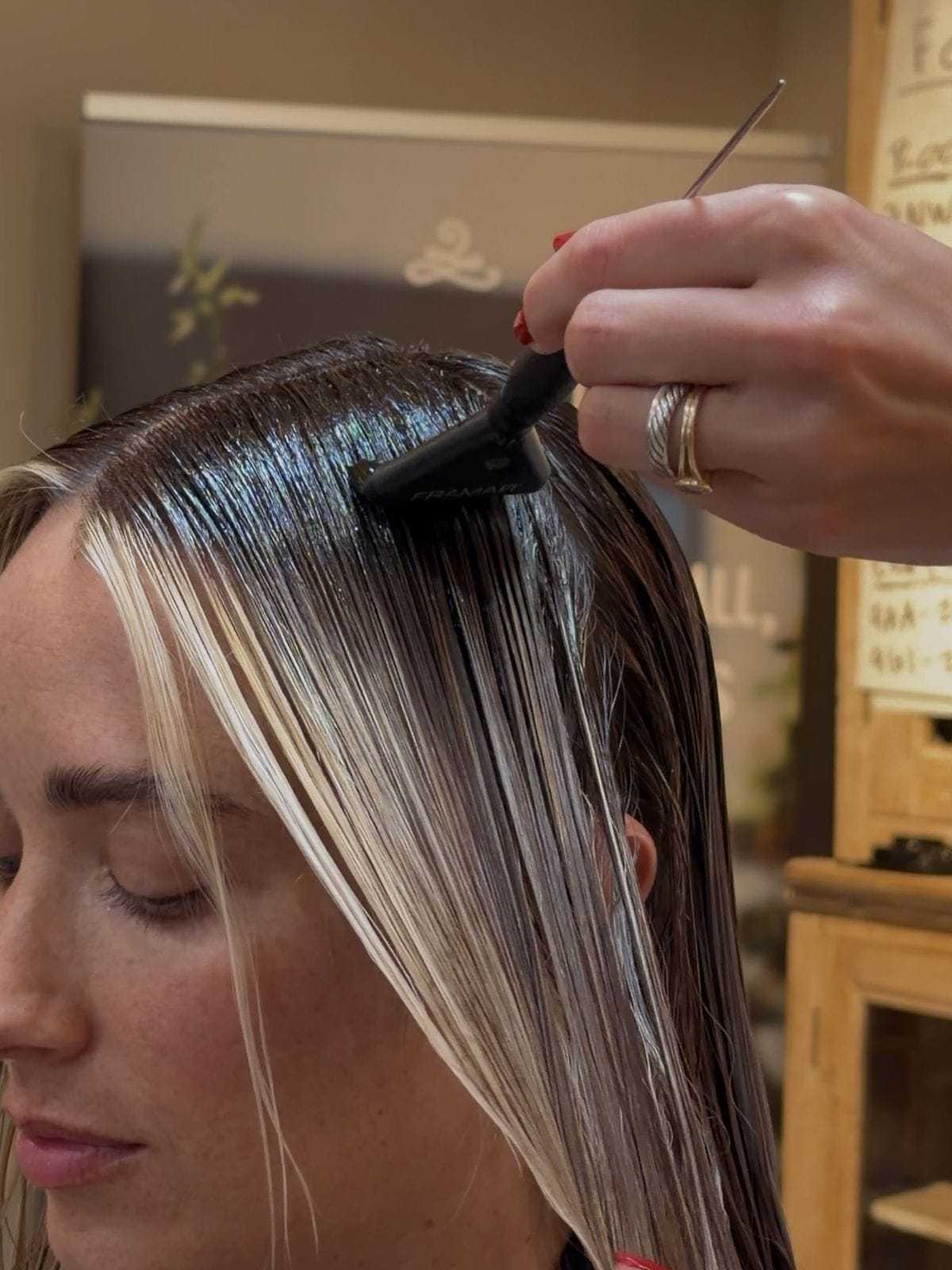Hair coloring in progress, dark dye applied to roots of a woman with light highlights.