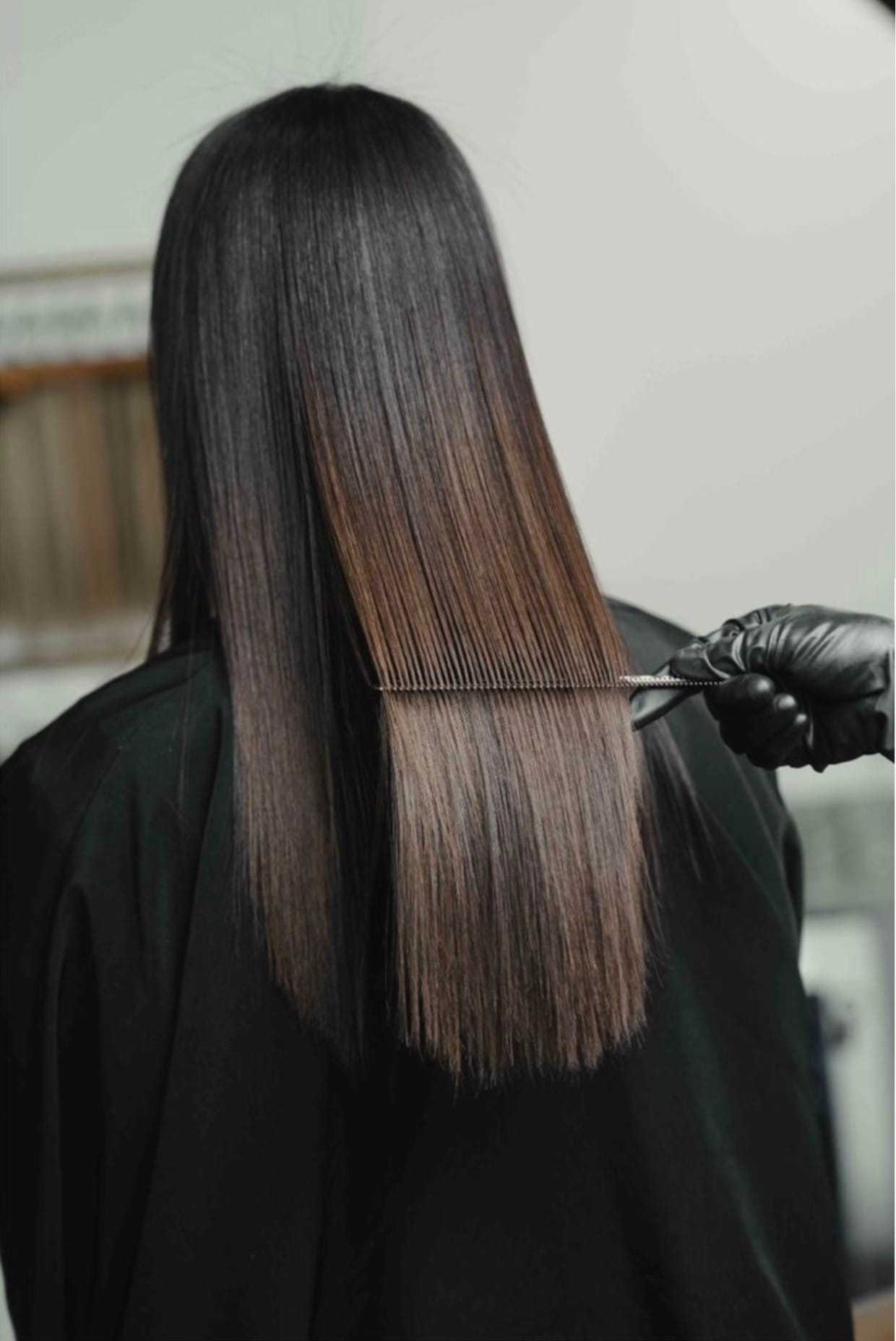 Hairdresser combing long, straight, brown hair with black gloves in a salon setting.