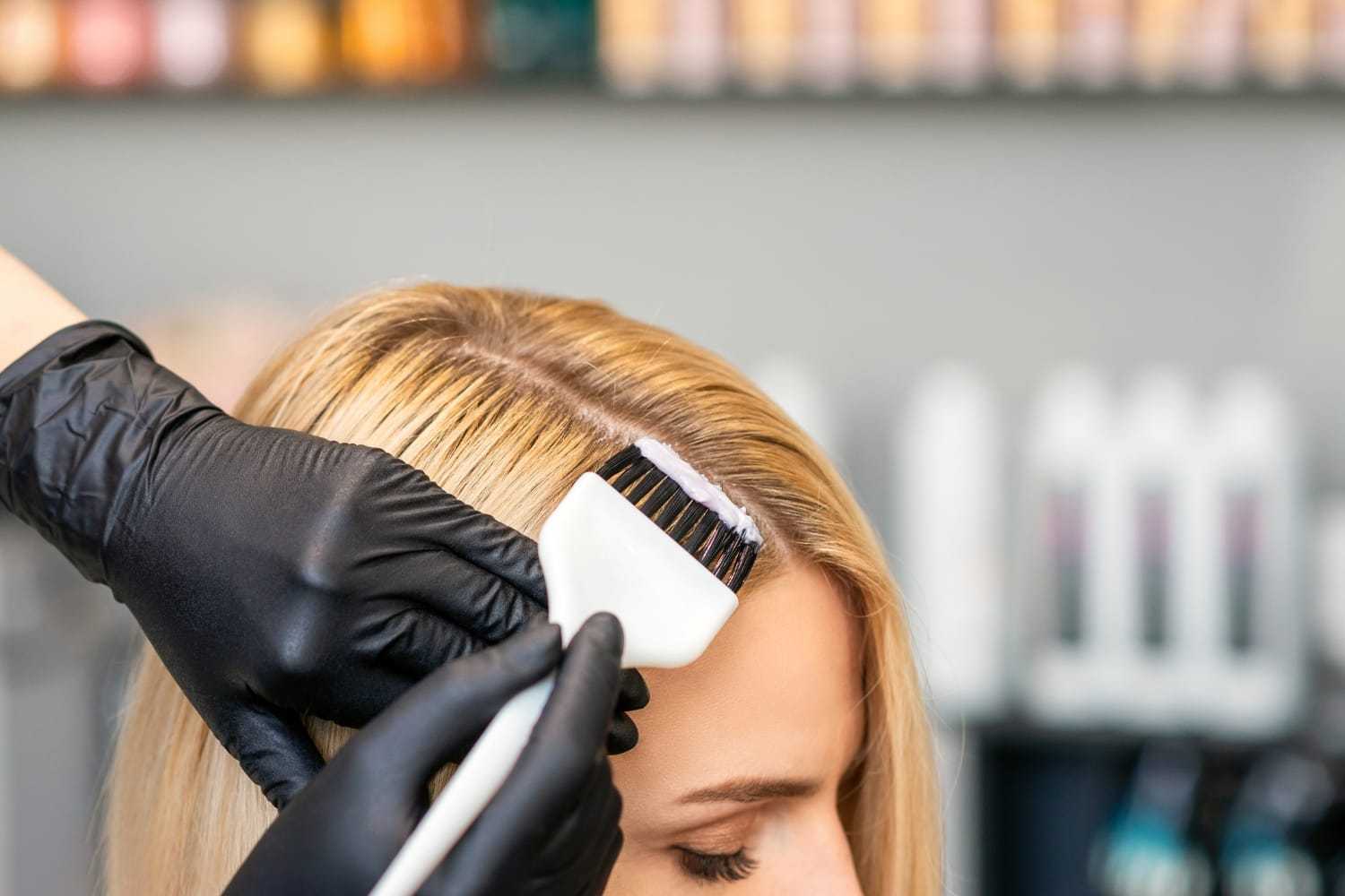 Hairdresser applying dye to blonde hair with a brush in a salon setting.