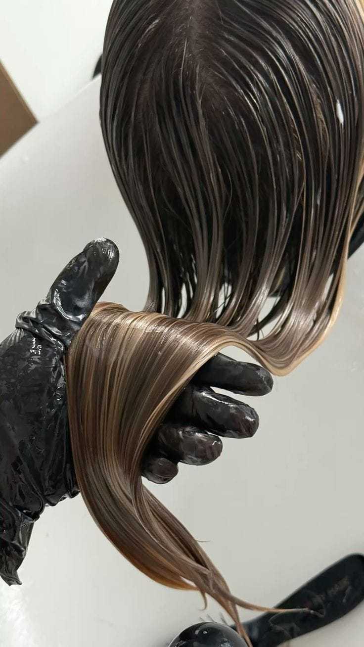 Hair coloring process with gloved hand holding wet, freshly dyed brown hair.